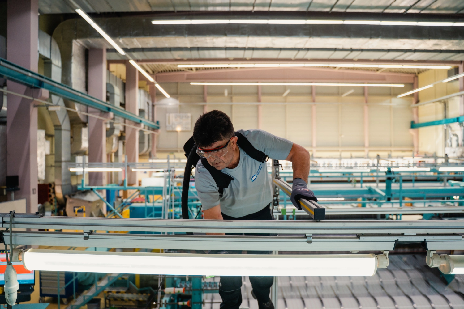 CleanFix Service Industriereinigung Förderband Halle Reinigungskraft mit Schutzbrille reinigt Förderband in einer Industriehalle — CleanFix Service Industriereinigung