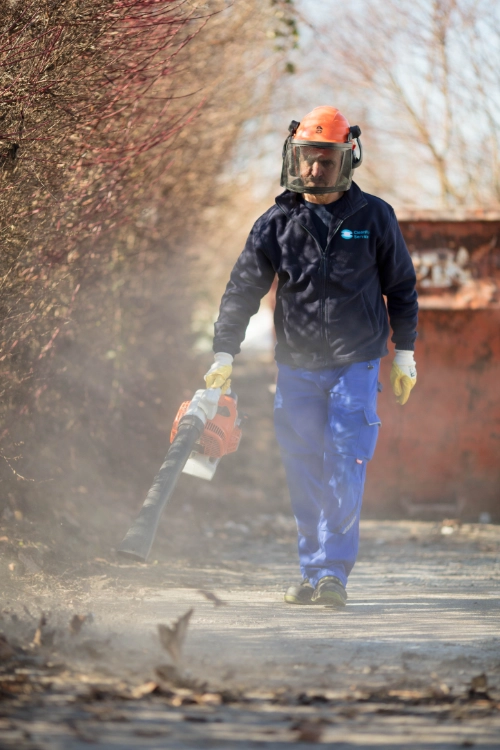 CleanFix Service Mitarbeiter mit Helm und Schutzvisier arbeitet mit Laubbläser bei Grünpflege