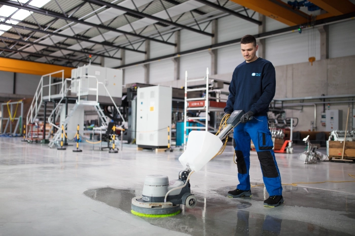 CleanFix Service Hallenreinigung Einscheibenmaschine Hallenboden Reiniger scheuert Hallenboden mit Einscheibenmaschine in einer Industriehalle — CleanFix Service